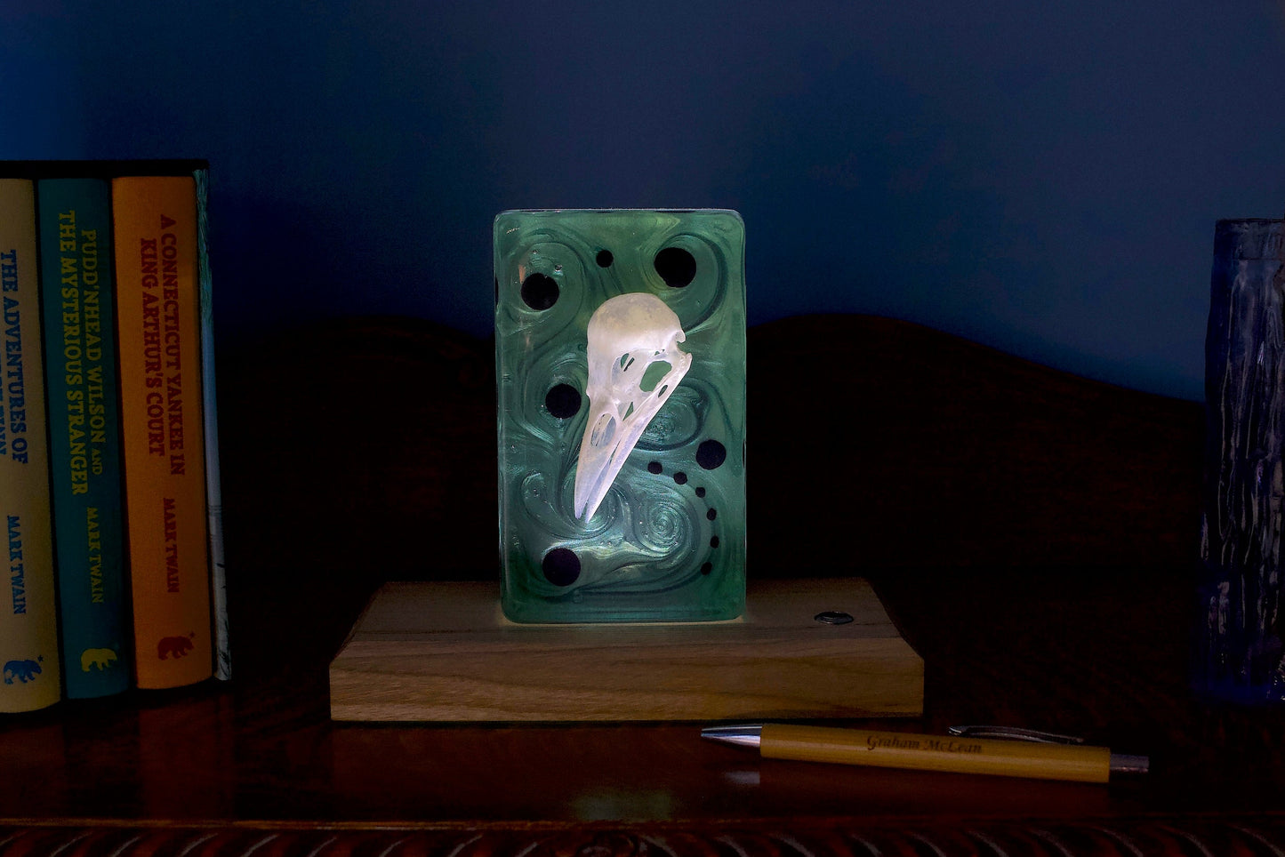 Bird skull in resin. Illuminated against a rich violet background. On a timber base